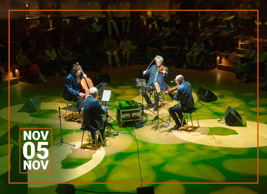 A live concert setting with musicians in the center of a warmly lit venue. A cellist, violist, and two violinists perform to an audience seated in a surrounding circular arrangement. The floor projects a vibrant green pattern, with stage equipment like speakers and monitors scattered around. The ambiance exudes intimacy and engagement between the performers and the captivated audience. In the bottom left corner is a box indicating the date "November 5."