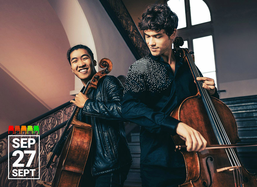 Two young cellists, one smiling brightly and the other focused on his instrument, stand on a grand staircase with ornate railings. Both hold their cellos and bows, dressed stylishly—one in a black leather jacket and the other in a dark shirt with silver embellishments. A large window and warm lighting create an inviting, elegant atmosphere. In the bottom left corner, the date "Sept 27" is prominently displayed.
