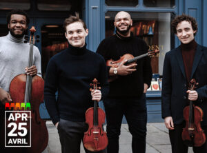 Four male string musicians stand outdoors in front of a blue storefront, each holding an instrument and smiling. From left to right: the first man wears a light grey turtleneck and holds a cello; the second wears a dark sweater and holds a viola; the third, dressed in black, holds a violin and smiles broadly; and the fourth, in a navy blazer and maroon turtleneck, also holds a violin. In the bottom left corner, white text reads "APR 25 AVRIL."