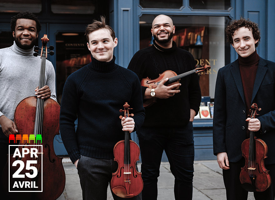 Four male string musicians stand outdoors in front of a blue storefront, each holding an instrument and smiling. From left to right: the first man wears a light grey turtleneck and holds a cello; the second wears a dark sweater and holds a viola; the third, dressed in black, holds a violin and smiles broadly; and the fourth, in a navy blazer and maroon turtleneck, also holds a violin. In the bottom left corner, white text reads "APR 25 AVRIL."