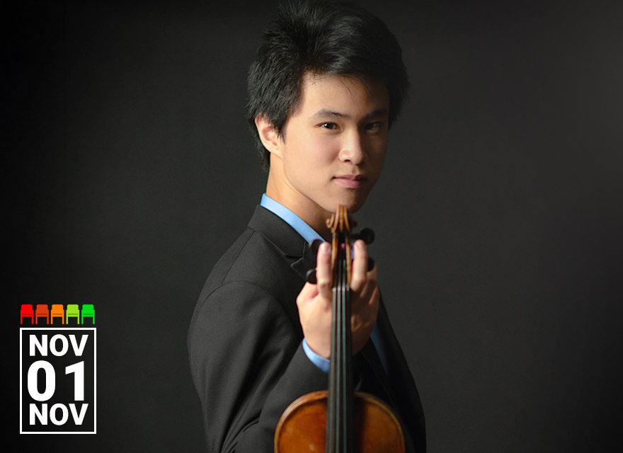 A young violinist dressed in a black suit with a light blue shirt poses confidently against a dark background. He gazes directly at the camera while holding his violin upright, with the scroll pointed forward. The dramatic lighting and poised expression create a sense of intensity and elegance. The date "Nov 01" is displayed in the bottom left corner.