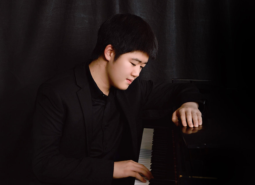 Violinist Irain Quirós, recipient of the 2025 Cecilia Concerts Developing Musician Award, poses with his violin against a dark background. He wears a black suit and holds the violin up near his shoulder while drawing the bow across the strings. His expression is calm and focused, and the image highlights both his face and the warm wood tones of the instrument. Promotional image of pianist Alex Yang seated at a grand piano in dark concert attire, looking down toward the keys against a black backdrop. At left, a graphic reads “MAY 16 / MAI 16” with a row of multicoloured chair icons above it.