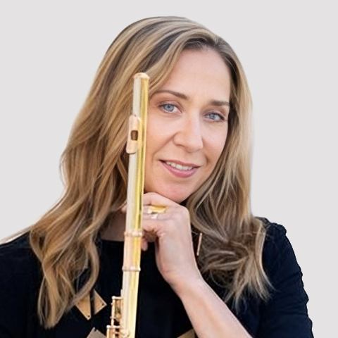 Marina Piccinini, a flautist with long blonde hair, holding her gold flute upright and looking toward the camera against a light grey background.