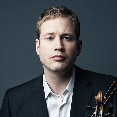 Portrait of violinist Jonathan Crow against a dark grey background. He is shown from the shoulders up, wearing a black suit jacket and a white dress shirt. He looks directly at the camera with a calm, focused expression. The scroll of his violin is partially visible over his right shoulder.