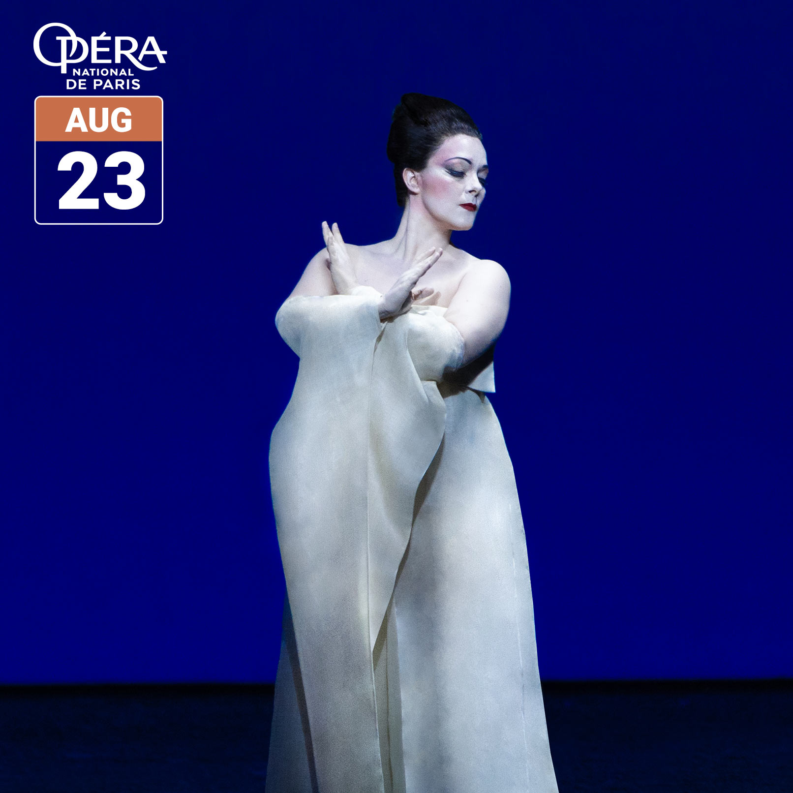 A performer in a white costume poses onstage against a deep blue background in a scene from Opéra national de Paris’ “Madame Butterfly.” The image includes the Opéra national de Paris logo and a date badge reading August 23.