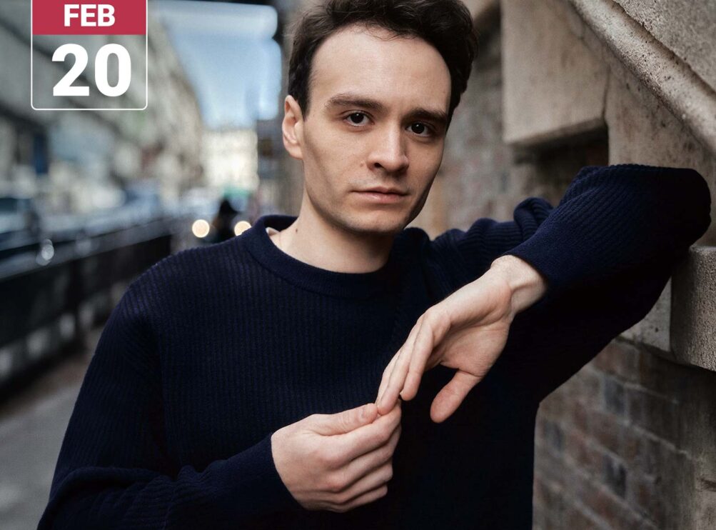 Concert graphic featuring pianist Jonathan Fournel in a navy sweater, leaning against a stone wall on a city street and looking toward the camera. His hands rest together in front of him. A white Main Stage Concerts logo and a red-and-white February 20 date badge appear in the upper left.