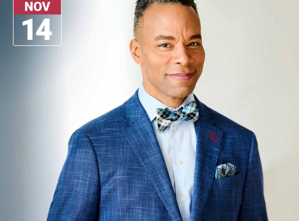 Portrait of a man wearing a blue plaid suit jacket, light blue shirt, and patterned bow tie against a light neutral background. A Main Stage Concerts graphic in the upper left displays the date November 14.