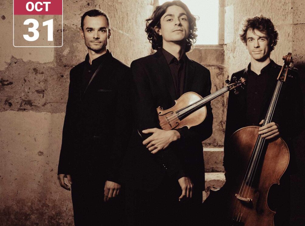 Trio Hélios members Alexis Gournel, Luka Ispir, and Raphaël Jouan pose with violin and cello in a stone interior, dressed in black.
