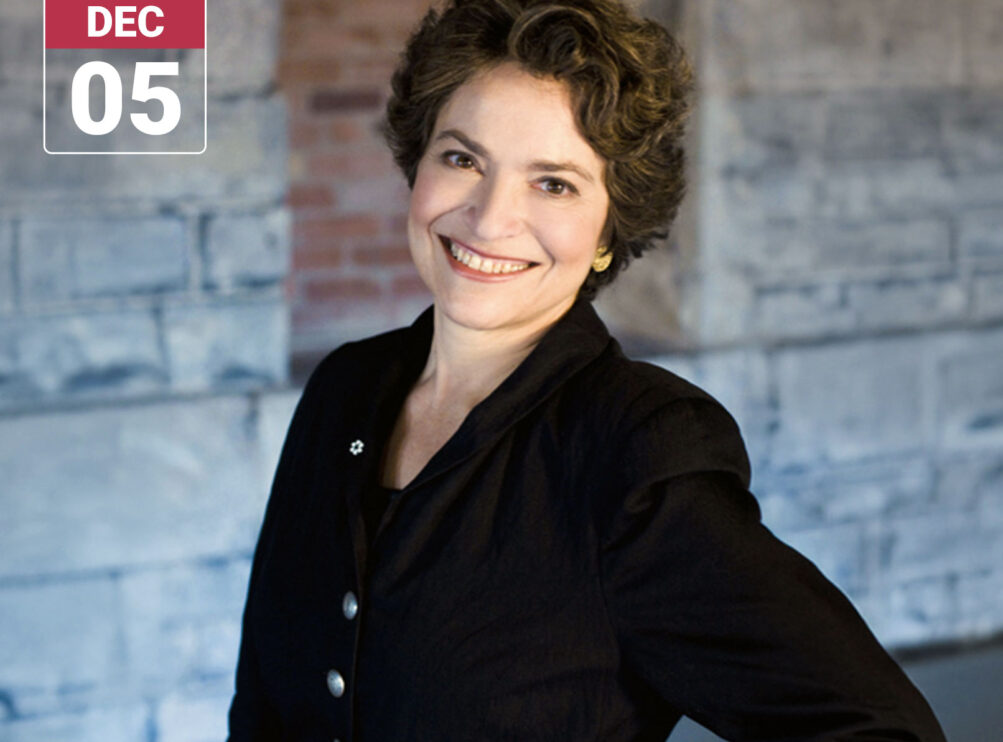 Baroque violinist Jeanne Lamon smiles at the camera, wearing a black jacket against a softly blurred stone and brick background. A graphic in the upper left reads “Main Stage Concerts” and “DEC 05.”